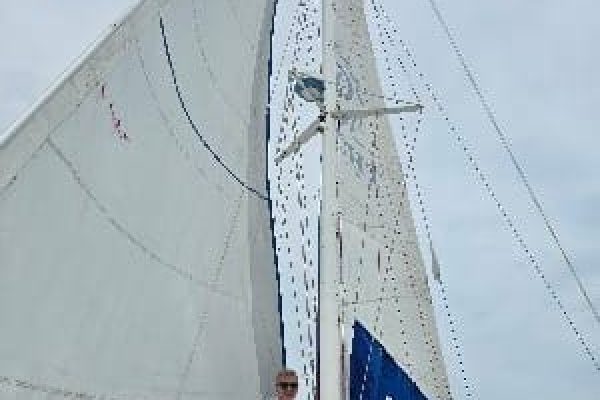 Young man in front of the white sails of a catamaran, with the vast sea and clear sky in the background.