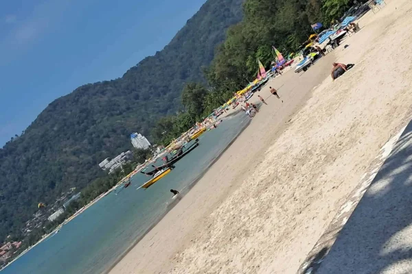 A vibrant scene at Patong Beach, Phuket, with beach goers relaxing and boats sailing in the turquoise water.