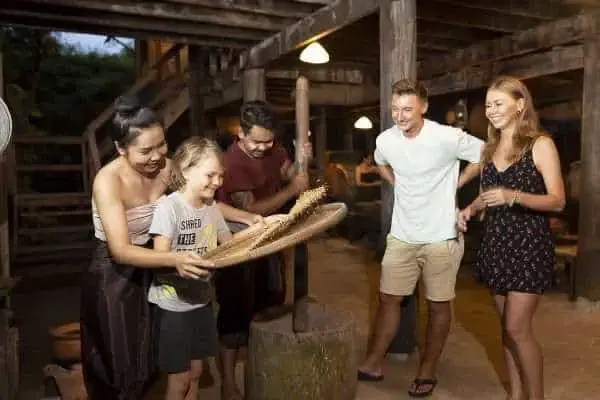 Eine Familie mit vier Personen genießt eine Mahlzeit an einem Holztisch bei der Siam Niramit Show in Phuket, umgeben von kultureller Atmosphäre.