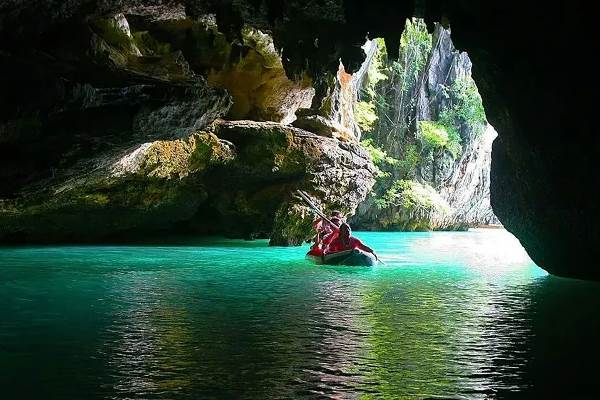 A man paddles a canoe through the tranquil waters of a cave, surrounded by rocky walls and dim lighting.