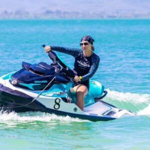 A woman confidently rides a jet ski across the vibrant blue ocean waves under a clear sky.