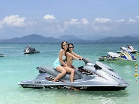 Two women on a thrilling jet ski ride in sparkling blue waters near Khai Island on a Phuket tour.
