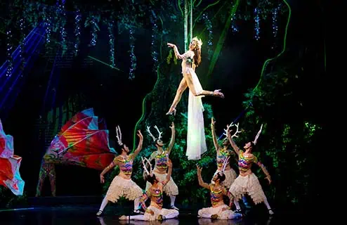 A woman in a colorful costume gracefully suspended in mid-air, highlighting her elegance and poise in a clear backdrop.