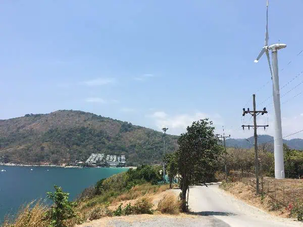 Wind turbines on a hillside overlooking Nai Harn Beach and the sea with scenic natural beauty.